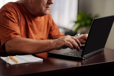 Téléchargez les photos : Image recadrée d'un homme âgé travaillant ou jouant à un jeu sur ordinateur portable - en image libre de droit