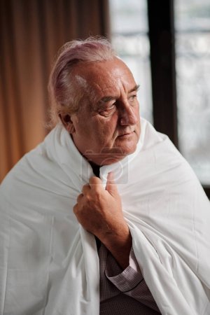 Photo for Portrait of freezing senior man wraping in duvet and looking away - Royalty Free Image