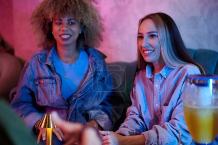 Téléchargez les photos : Joyeux jeunes femmes traînant avec des amis dans un pub - en image libre de droit