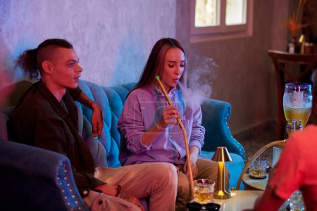 Téléchargez les photos : Jeune femme fumant narguilé en traînant avec des amis dans le bar - en image libre de droit