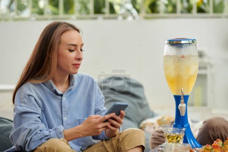 Téléchargez les photos : Sourire jeune femme textos lorsque vous buvez de la bière avec des amis - en image libre de droit