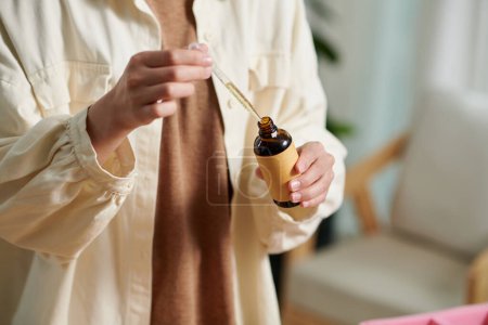 Téléchargez les photos : Hands of woman using pipette when taking essential oil from glass bottle - en image libre de droit