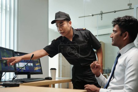 Téléchargez les photos : Gardien pointant vers l'écran de l'ordinateur lorsque vous regardez des vidéos de surveillance avec le gestionnaire - en image libre de droit