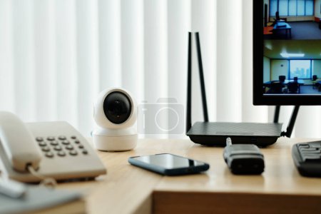 Photo for Surveillance camera, router and telephone next to monitor on desk of security guard - Royalty Free Image