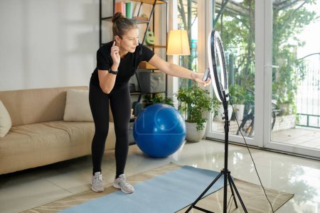 Téléchargez les photos : Instructeur de fitness en ligne réglage smartphone et lampe annulaire pour filmer des vidéos pour blog à la maison - en image libre de droit