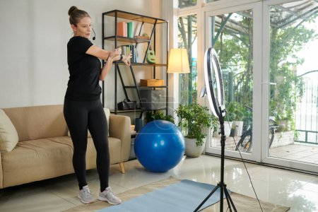 Téléchargez les photos : Fitness blogger recording herself stretching arms and warming up - en image libre de droit
