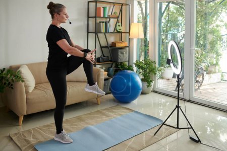 Téléchargez les photos : Fitness blogger filming herself warming up at home - en image libre de droit