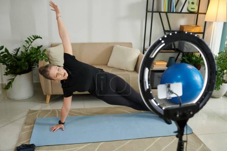 Téléchargez les photos : Online fitness instructor filming herself doing side plank - en image libre de droit