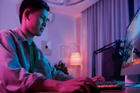 Foto de Teenage boy playing video game on computer in his neon bedroom - Imagen libre de derechos