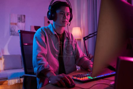 Téléchargez les photos : Portrait of teenage gamer playing videogame on computer in neon bedroom - en image libre de droit
