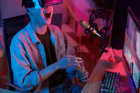 Téléchargez les photos : Emotional lets player drinking iced coffee when recoding himself playing video game in virtual reality headset - en image libre de droit