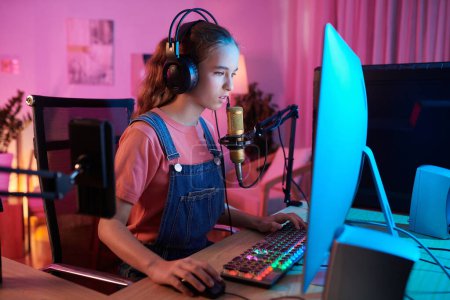 Téléchargez les photos : Adolescent fille streaming vidéo de elle-même jouer jeu vidéo dans néon chambre - en image libre de droit