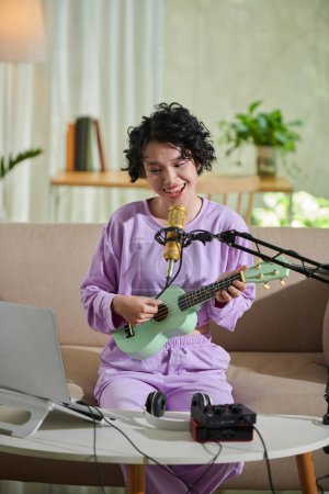 Téléchargez les photos : Joyeux adolescent fille enregistrement elle-même jouer ukulele et chanter - en image libre de droit
