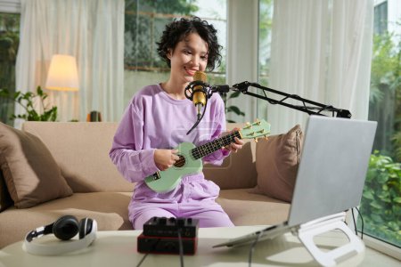 Téléchargez les photos : Adolescente souriante chantant dans le micro et jouant ukulele - en image libre de droit