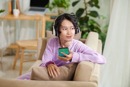 Téléchargez les photos : Souriant adolescent fille profiter de la musique de sa liste de lecture sur smartphone - en image libre de droit