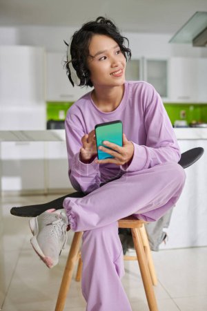 Téléchargez les photos : Portrait of happy teenage girl in lavender tracksuit turning on energetic music on smartphone - en image libre de droit