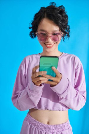 Photo for Cheerful teenage girl in clear glasses texting best friends - Royalty Free Image