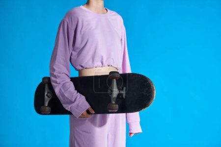 Téléchargez les photos : Cropped image of girl in lavender top and higher holding skateboard - en image libre de droit