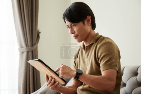 Téléchargez les photos : Portrait of serious young man reading article on digital tablet - en image libre de droit