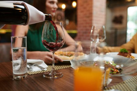 Téléchargez les photos : Restaurant sommelier pouring red wine in glass for woman - en image libre de droit