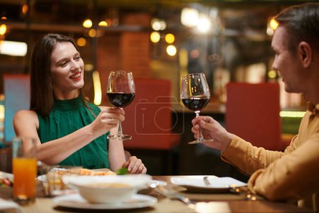 Téléchargez les photos : Happy couple griller avec des verres de vin rouge lorsque vous êtes assis à la table du dîner - en image libre de droit