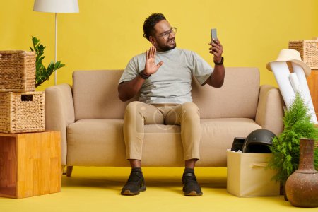 Photo for Smiling man sitting on couch and video calling friend or family member - Royalty Free Image