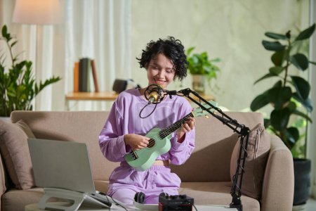Téléchargez les photos : Smiling teenage girl recording herself playing ukulele and singing - en image libre de droit