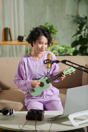Photo for Joyful teenage girl streaming herself singing song and playing ukulele - Royalty Free Image