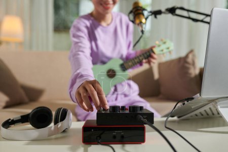 Photo for Closeup image of teenage girl turning up volume on amplifier when recording herself playing ukulele - Royalty Free Image
