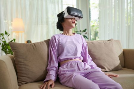 Téléchargez les photos : Amazed teenager in lavender homewear watching video in VR headset - en image libre de droit