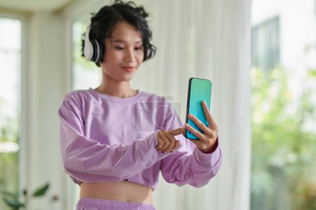 Téléchargez les photos : Teenage girl choosing music track from playlist to listen to in headphones - en image libre de droit