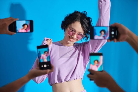 Téléchargez les photos : Happy teenage blogger posing when subscribers photographing her on smartphones - en image libre de droit