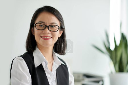 Téléchargez les photos : Portrait of smiling social worker in glasses standing in office and looking at camera - en image libre de droit