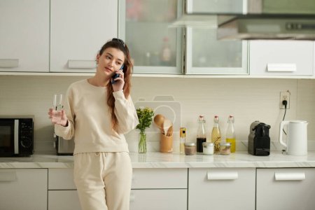 Téléchargez les photos : Young woman drinking water and talking on phone with friend - en image libre de droit