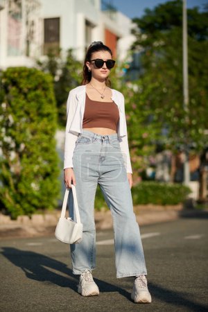 Téléchargez les photos : Young woman in wide jeans, sunglasses and white cardigan - en image libre de droit