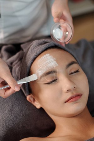 Photo for Esthetician applying moisturizing mask on face of young woman - Royalty Free Image