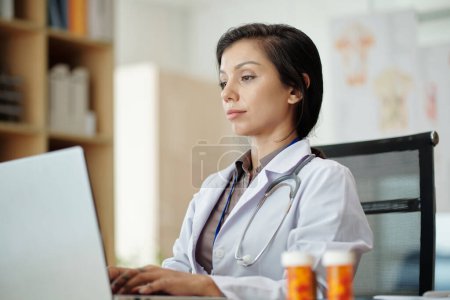 Téléchargez les photos : Formulaire de remplissage de médecin sur ordinateur portable lors de la rédaction de la prescription pour le patient - en image libre de droit