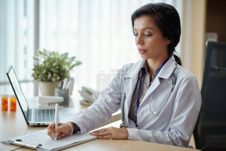 Téléchargez les photos : Médecin rédigeant la prescription après avoir eu une séance de télémédecine avec le patient - en image libre de droit