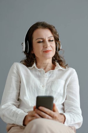 Photo for Happy mature woman closing eyes when enjoying good music from playlist on her smartphone - Royalty Free Image
