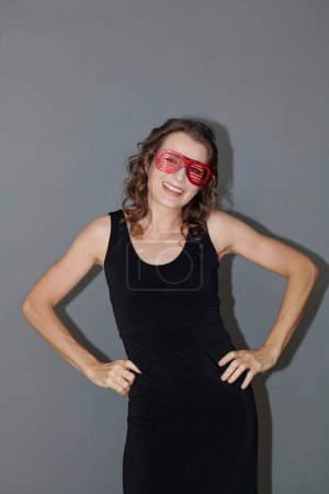 Photo for Happy mature woman in tight black dress and funny glasses dancing at party - Royalty Free Image
