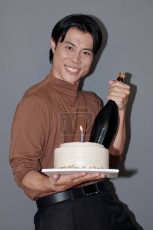 Téléchargez les photos : Portrait d'homme asiatique joyeux avec gâteau d'anniversaire et bouteille de champagne - en image libre de droit