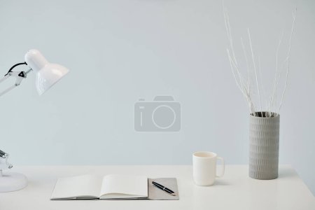 Foto de Planificador abierto, taza de café, lámpara y jarrón con ramas en la mesa - Imagen libre de derechos