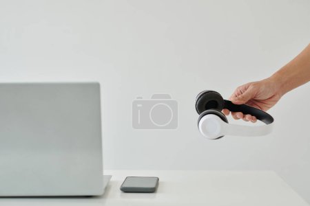 Foto de Mano de hombre de negocios poniendo auriculares en el escritorio de la oficina con el ordenador portátil y teléfono inteligente - Imagen libre de derechos