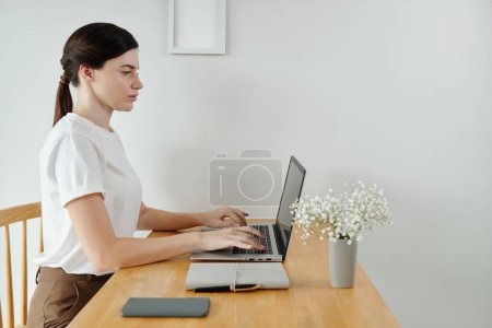Foto de Mujer joven seria que trabaja en el ordenador portátil en el escritorio en su oficina en casa - Imagen libre de derechos