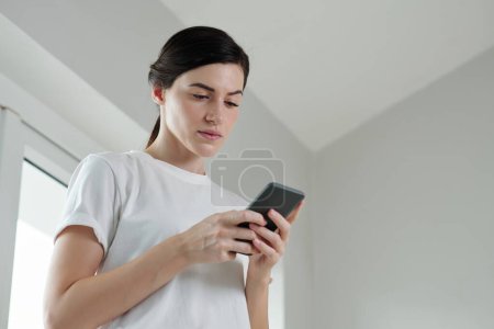 Foto de Mujer joven seria leyendo la notificación en el teléfono inteligente - Imagen libre de derechos