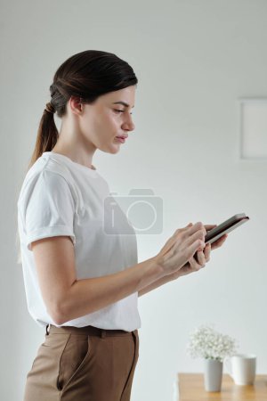 Téléchargez les photos : Jeune femme en t-shirt blanc de base envoyer des messages texte à un collègue - en image libre de droit