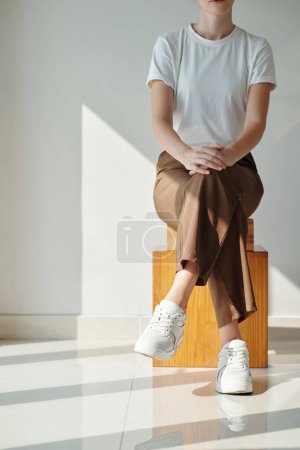 Foto de Imagen recortada de mujer joven en camiseta blanca lisa sentada en caja de madera - Imagen libre de derechos