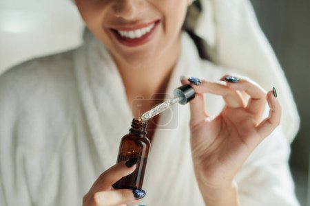 Photo for Happy woman in bathrobe opening vial with moisturizing essence - Royalty Free Image