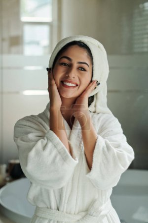 Téléchargez les photos : Portrait de jeune femme joyeuse en peignoir et serviette sur la tête debout dans la salle de bain - en image libre de droit