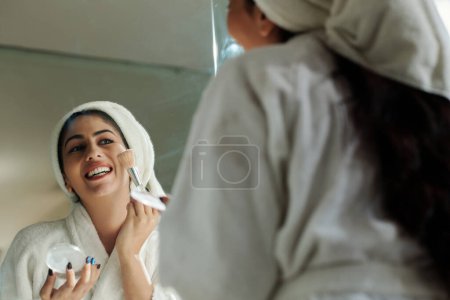 Photo for Joyful young woman in bathrobe applying face powder - Royalty Free Image